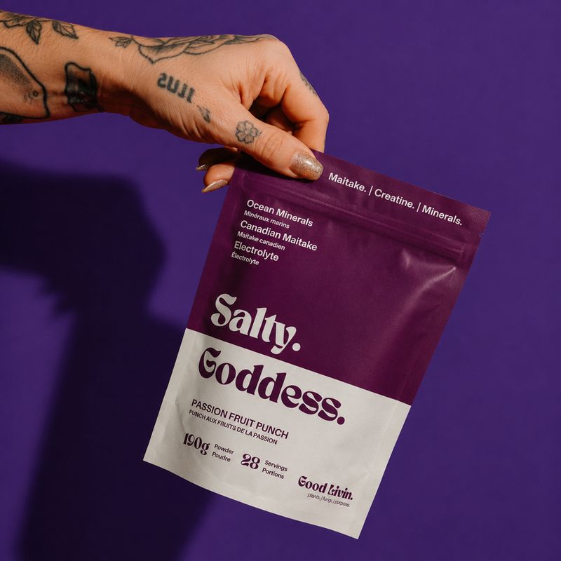 Hand holding a bag of Salty Goddess against a purple wall